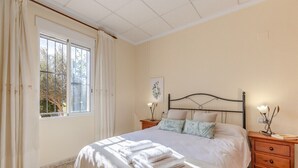 Une chambre à coucher comprenant un lit, deux tables de chevet, une fenêtre avec des rideaux et un tableau accroché au mur.