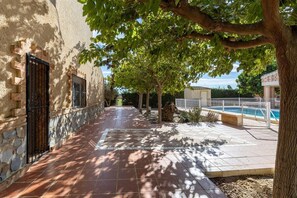 Ein Innenhof mit einer gefliesten Terrasse, einem Schwimmbecken und einem Baum, der Schatten spendet.