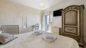 A bedroom with a bed, a dresser, a mirror, a radiator, and a television on the wall.