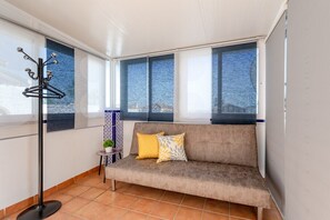 A room with a sofa, a coat rack, a small table with a plant, and large windows with a view. - Infinity Haven by Fidalsa (Orihuela)