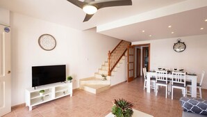 A living room with a TV, staircase, dining area, and a ceiling fan. - Golden Coast Retreat by Fidalsa (Creixell)