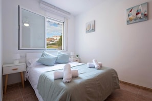 A bedroom with a bed, a nightstand, a window, and a painting on the wall. - Golden Coast Retreat by Fidalsa (Creixell)
