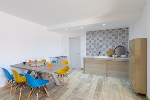 Une cuisine moderne avec un mur recouvert de carreaux, un coin repas avec une table et des chaises, et une porte donnant sur une autre pièce.