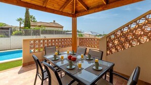 A covered outdoor dining area with a pool view, wooden ceiling, and a decorative fence. - Mountain Beautiful by Fidalsa (Busot)