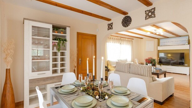 A dining area with a wooden ceiling, a white cabinet with glass doors, and a sofa in the background. - Mountain Beautiful by Fidalsa (Busot)