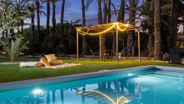A swimming pool with a pergola and string lights, surrounded by palm trees. - Historical Palms by Fidalsa (Elche)