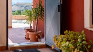 Une porte donnant sur un balcon agrémenté de plantes en pot et offrant une vue sur le ciel et le paysage.