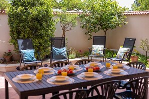 Un patio al aire libre con una mesa preparada para el desayuno, rodeado de sillas con cojines.