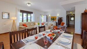 Un coin repas avec une longue table dressée pour six personnes, un canapé et, au fond, une cuisine.