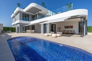 Ein modernes, zweistöckiges Haus mit Swimmingpool, Sitzgelegenheiten im Freien und einem draußen abgestellten Fahrrad.