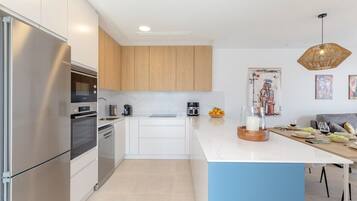 A modern kitchen with stainless steel appliances, wooden cabinets, a marble countertop, and a dining area with a table set for two.