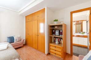 A bedroom with a bed, a wardrobe, a shelf with books and a plant, and a bathroom with a mirror and sink. - Flamenca Beach by Fidalsa (Orihuela)