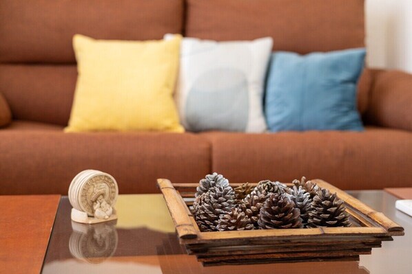 A wooden tray with pine cones on a reflective surface, a small decorative item, and a brown sofa with three pillows in the background. - Flamenca Beach by Fidalsa (Orihuela)