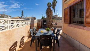 Un patio al aire libre con una mesa, sillas, una palmera y un edificio con una ventana.