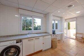 Une cuisine moderne équipée d’un lave-linge, d’un évier et de grandes fenêtres.