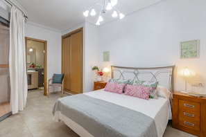 Quarto com cama, mesas de cabeceira, uma cadeira, guarda-roupa e banheiro visível através de uma porta aberta.