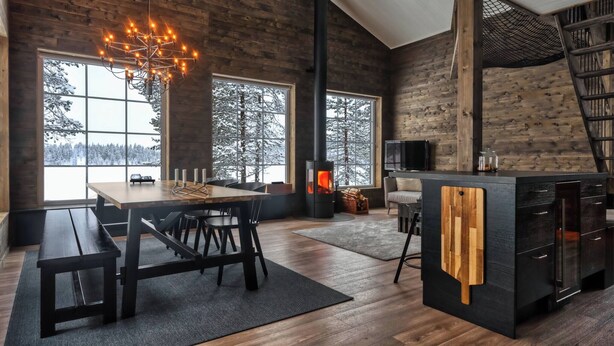 Ein modernes Interieur mit einem Holzesstisch, Bänken, einem Kamin und großen Fenstern.