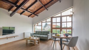 Amplia sala de estar con techo de madera, ventanas grandes, un sofá, una mesa de comedor y un televisor montado en la pared.