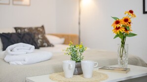 A neatly made bed with folded white towels, a bedside table with two white mugs and a small potted plant, and a vase with yellow flowers. - Coral Seashell by Fidalsa (Guardamar del Segura)