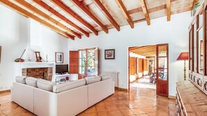 A spacious living area with a sofa, TV, fireplace, and wooden beams. - Villa 'Martorell' with Private Pool, Wi-Fi and Air Conditioning (Illes Balears)