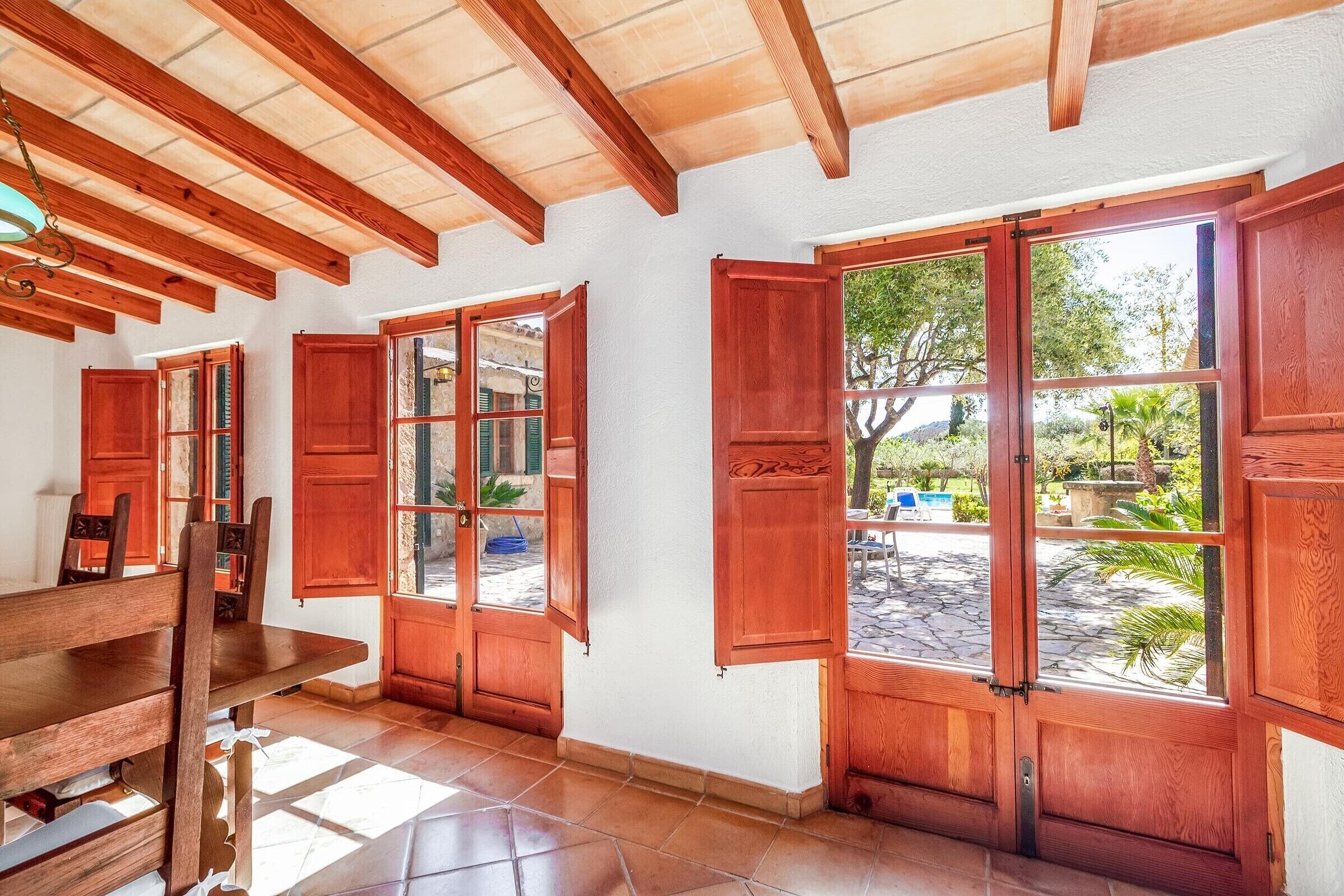 A room with wooden beams, a dining table, and large windows with wooden shutters.
