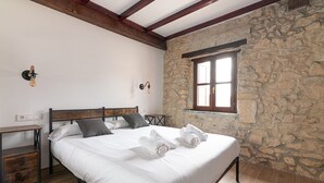 Een slaapkamer met een stenen muur, een houten bed, een nachtkastje en een raam met uitzicht.