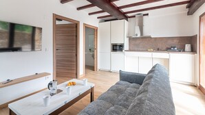 Ein modernes Wohnzimmer mit einer Couch, einem Couchtisch mit Tassen und einer Kaffeemaschine, sowie einer Küchenzeile mit weißen Schränken und einer Mikrowelle.