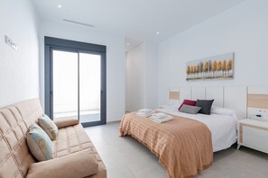 A modern hotel room with a bed, a sofa, a painting, and a view through a glass door. - Fidalsa 5 Stars Sea Views (Rojales)