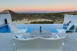 A terrace with white lounge chairs, a table with wine glasses, and a view of a desert landscape at sunset. - Fidalsa 5 Stars Sea Views (Rojales)