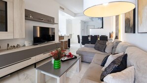 Ett modernt vardagsrum med en soffa, ett soffbord, en tv och en matplats i bakgrunden.