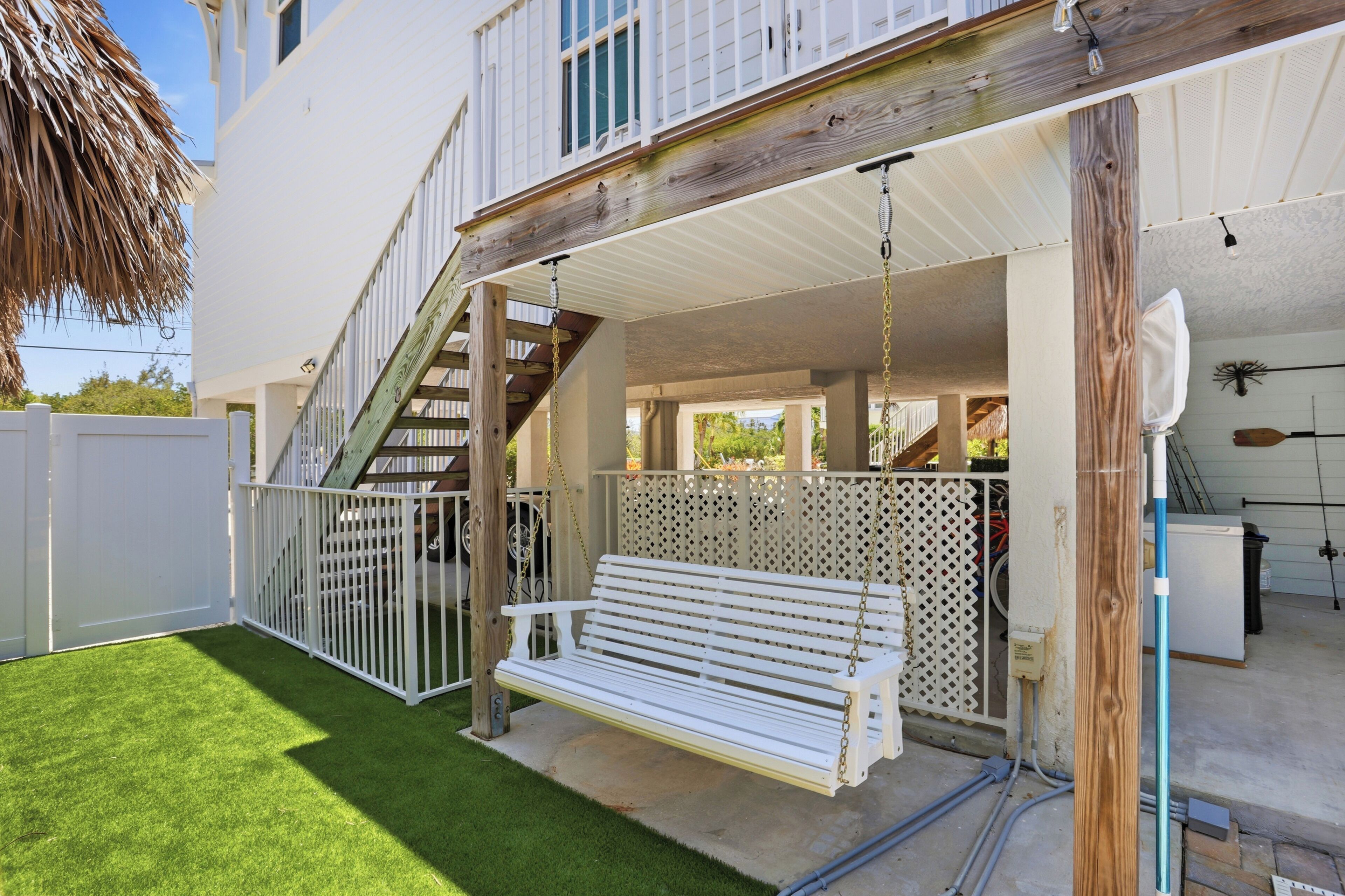 A covered outdoor area with a wooden bench, a white fence, and a staircase leading to an upper level.