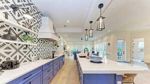 A modern kitchen with a central island, blue cabinetry, patterned backsplash, and pendant lighting. - Pineapple Paradise-Pool Home 2Blocks to the Beach-By Island Real Estate (Holmes Beach)