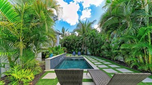 A swimming pool with two wicker lounge chairs, surrounded by lush greenery and a clear sky. - Pineapple Paradise-Pool Home 2Blocks to the Beach-By Island Real Estate (Holmes Beach)