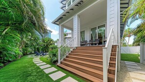 A house with a wooden staircase leading to a porch, surrounded by lush greenery and a well-maintained lawn. - Pineapple Paradise-Pool Home 2Blocks to the Beach-By Island Real Estate (Holmes Beach)