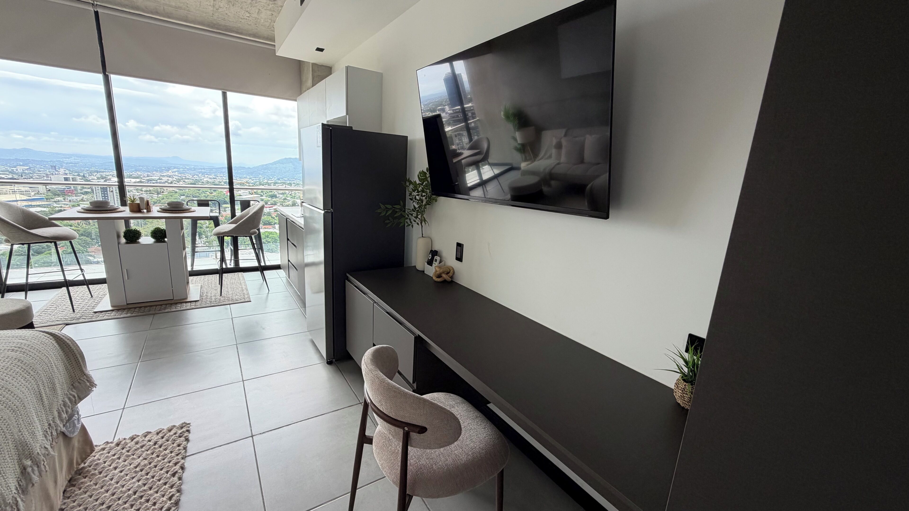 Une chambre d’hôtel moderne dotée d’une grande télévision, d’un balcon avec vue sur la ville, d’un coin repas et d’un lit.
