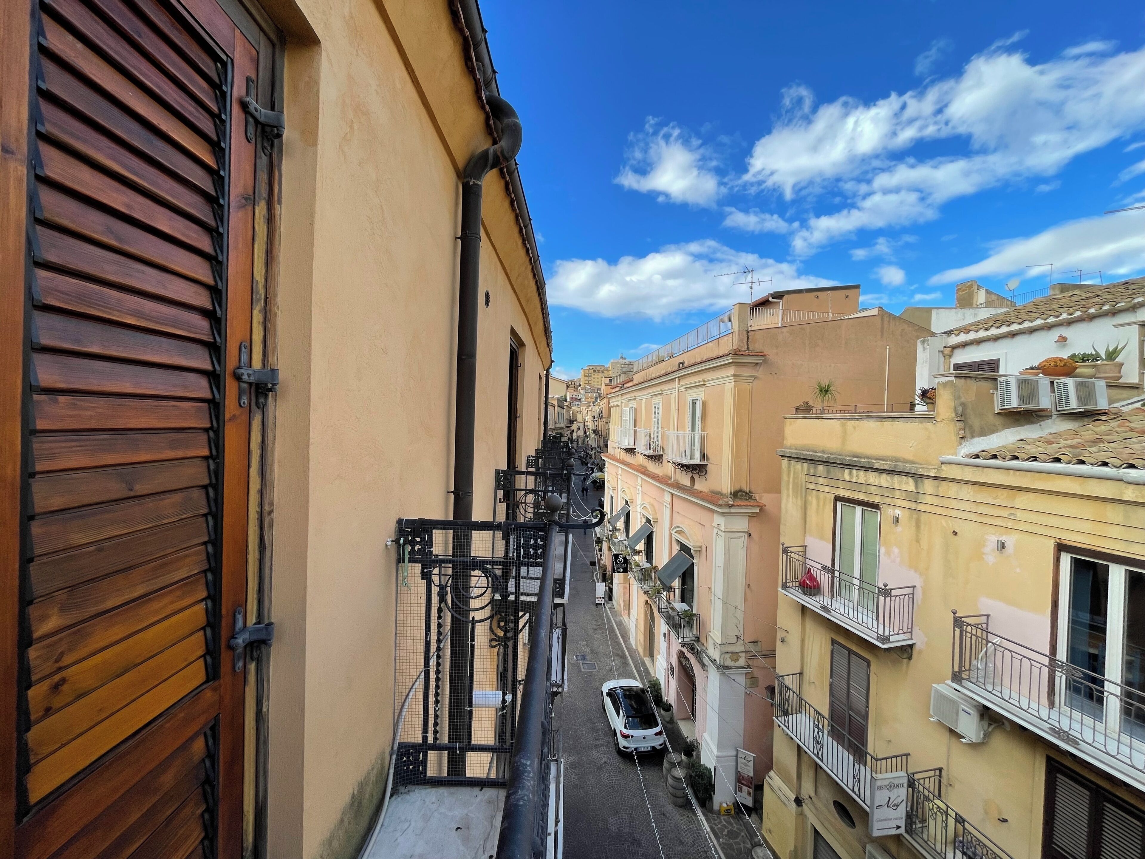 A narrow street with buildings on both sides, a parked car, and a visible electrical box.