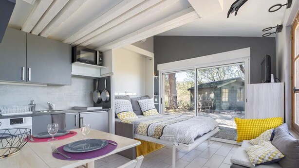 Una cocina moderna con microondas, mesa de comedor con platos y vasos, y una cama con almohadas.