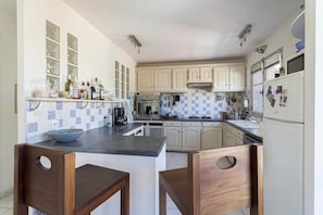 Una cocina con armarios blancos, salpicadero de azulejos, cafetera y refrigerador.