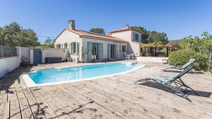 Una casa con piscina, mobiliario de jardín y una terraza de madera.