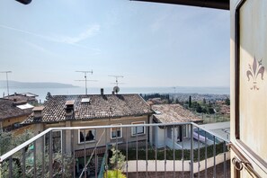 Ein Wohngebiet mit Ziegeldächern, einem Balkon mit Metallgeländer und Blick auf das Meer und die entfernten Hügel.