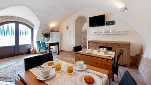 A dining area with a table set for breakfast, a television mounted on the wall, and a kitchen area visible in the background.