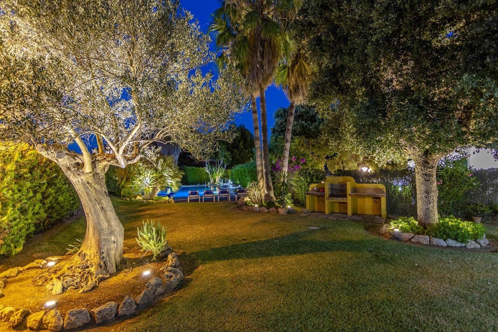 A well-lit outdoor area with a pool, lounge chairs, and a stone pathway.