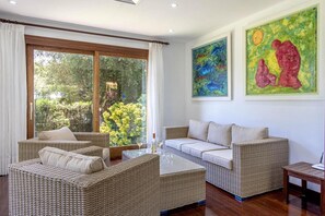 A room with wicker furniture, a glass coffee table, and artwork on the walls. - Holiday Home "Formosa" with Pool, Wi-Fi, Air Conditioning & Garden (Cala de Sant Vicenç)
