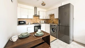 A compact kitchen with white cabinets, a stainless steel refrigerator, a microwave, a stove, and a washing machine. - Chic 1BR West Ealing - 15m Heathrow - 20m City (London)