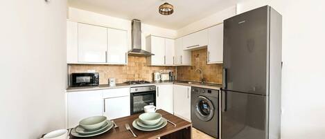 A compact kitchen with white cabinets, a stainless steel refrigerator, a microwave, a stove, and a washing machine.