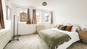 A bedroom with a bed, a radiator, a window with curtains, a standing lamp, and a view of buildings outside. - Chic 1BR West Ealing - 15m Heathrow - 20m City (London)