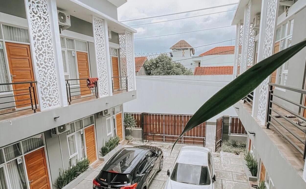 A courtyard with two cars parked, a white building with patterned columns, and a view of neighboring houses.