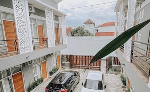 A courtyard with two cars parked, a white building with patterned columns, and a view of neighboring houses.