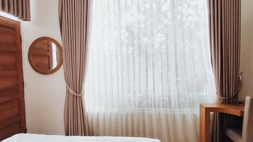 Ein Schlafzimmer mit einem Bett, einem runden Spiegel, einem Holztisch und einem Fenster mit Vorhängen.