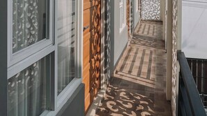 Un couloir avec des portes décorées, un sol carrelé et un balcon doté d’une balustrade.